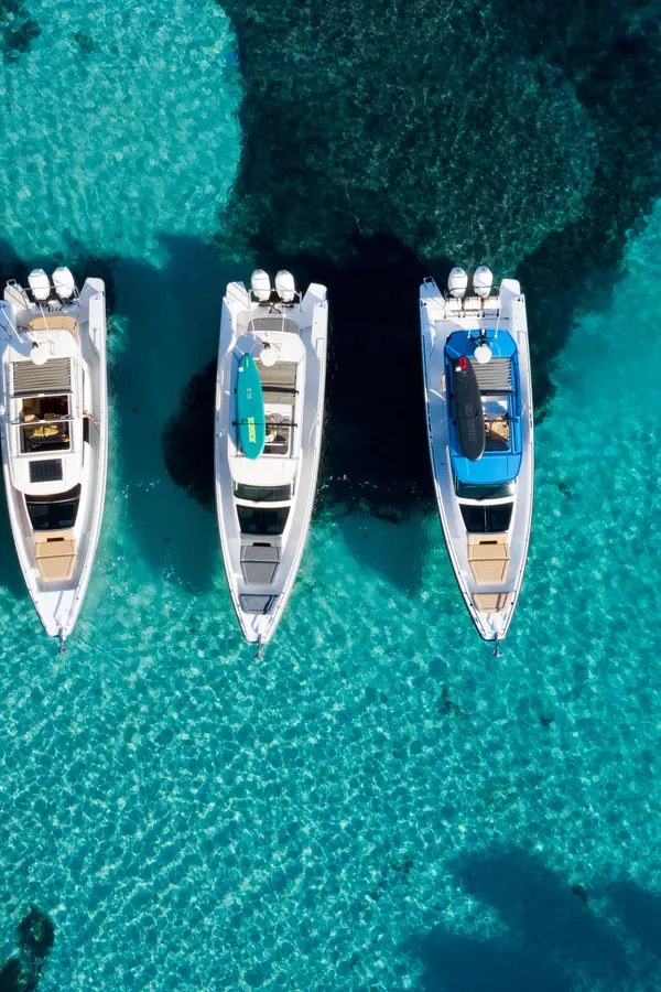 Modern motorboats, including the Axopar 37 model, anchored in calm, clear blue waters along the Cretan coast.